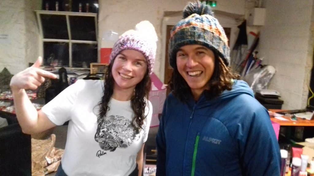 A girl with a white t-shirt with a logo on a brain on. She is stood next to a man who's last name is Brain. Both are wearing excellent bobble hats.