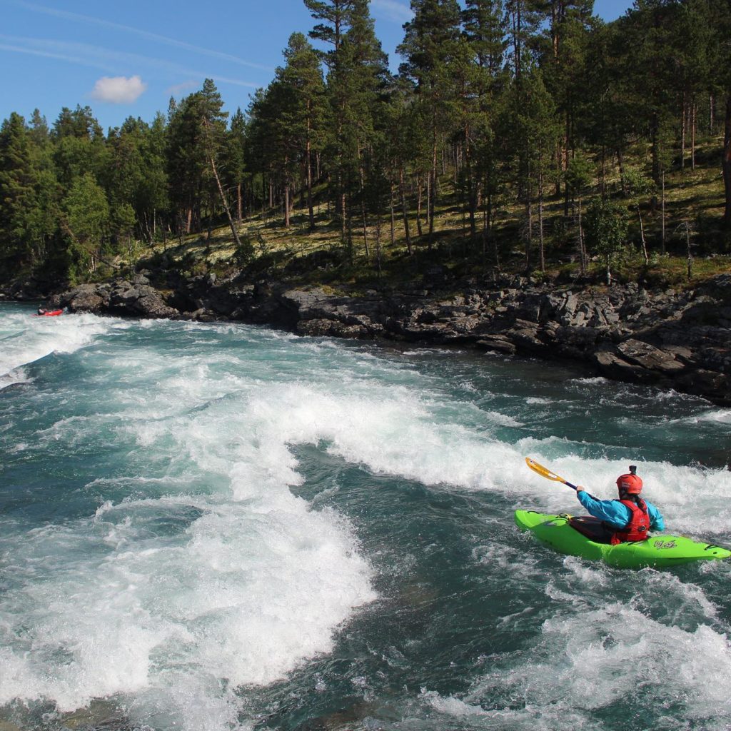 A girl in a green kayak paddling down a river. She is about to hit a wave train.